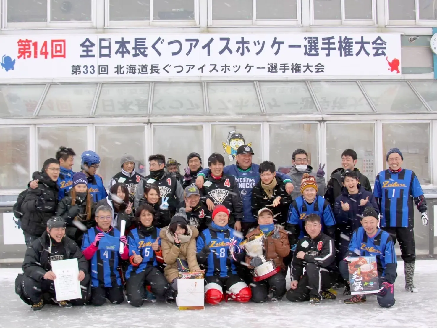 全日本長ぐつアイスホッケー選手権大会の看板の前で記念撮影する選手たち