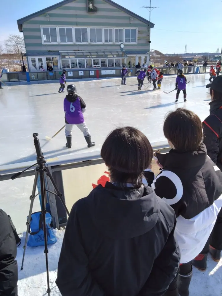 北海道釧路町の屋外リンクで行われる試合と、それを見守る選手たち